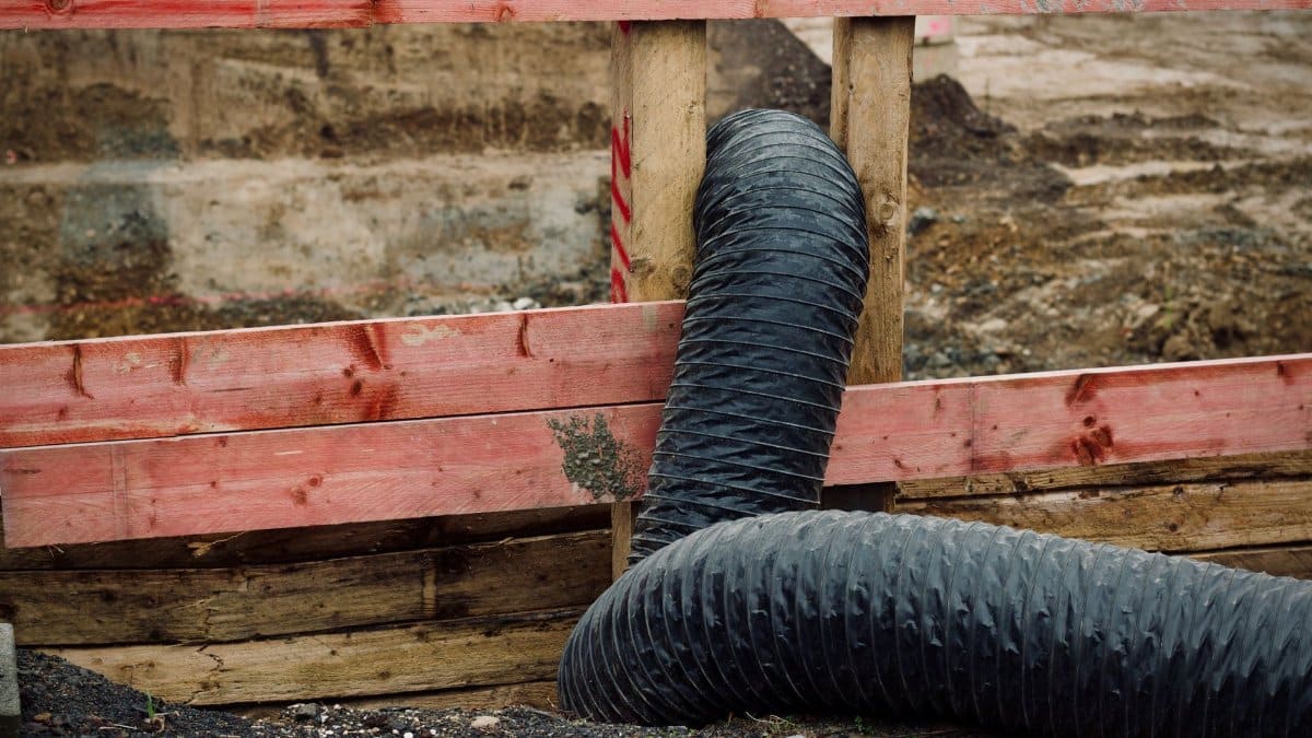 Close-up of a construction site showing red wooden barriers and a flexible black duct.