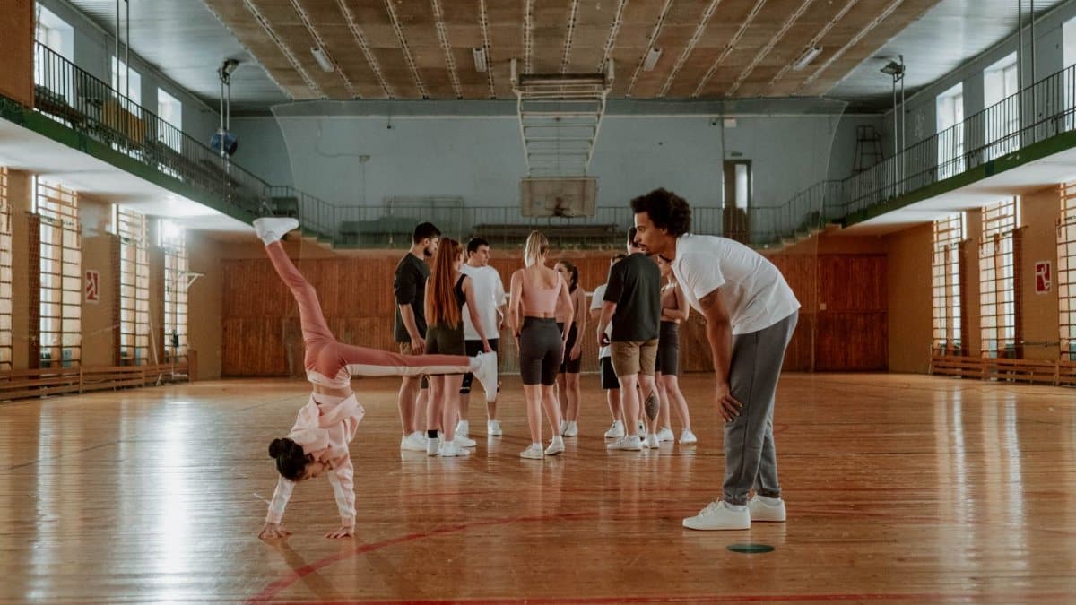 Young girl practicing gymnastics in a lively indoor gym environment with a coach.