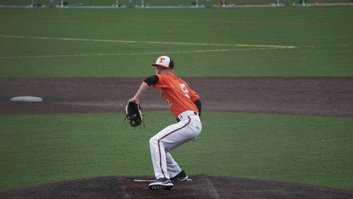 A baseball player in action, pitching on a sports field wearing an orange jersey.