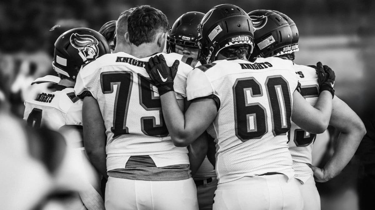 High school football team players huddle in a moment of unity before the game, emphasizing teamwork and strategy.