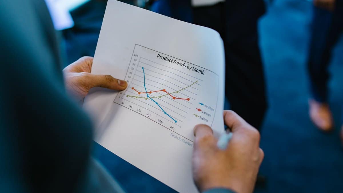 Close-up of hands holding a paper with a line graph showing product trends by month during a business meeting.