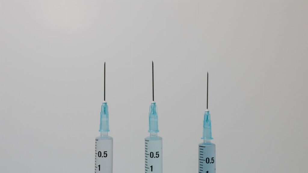 Close-up image of three syringes with needles against a neutral background.