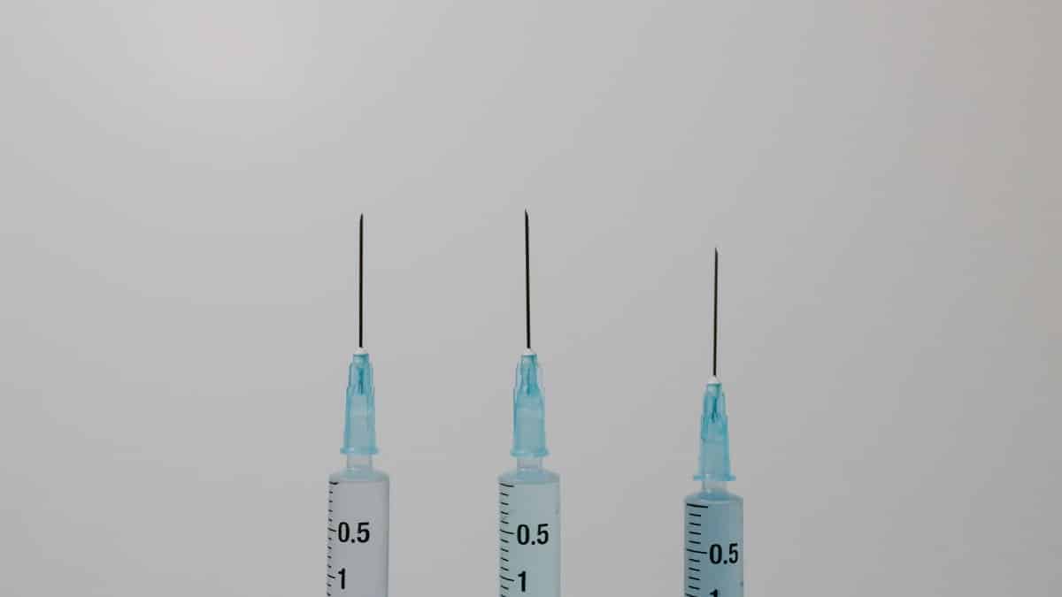 Close-up image of three syringes with needles against a neutral background.