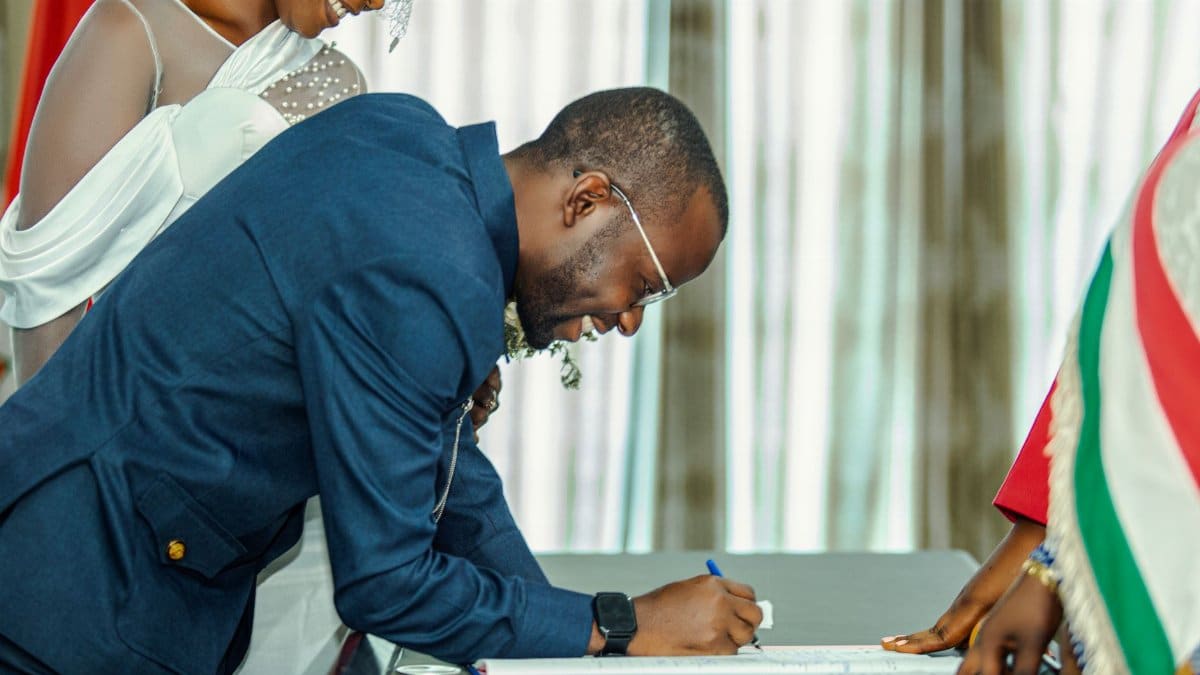 A groom signing a document at a wedding ceremony, with the bride joyfully looking on. Intimate and elegant moment.
