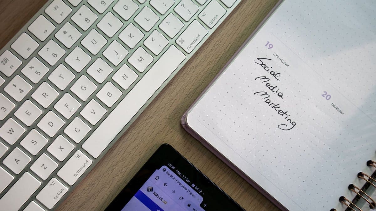 Top view of keyboard, planner with social media marketing note, and tablet on a desk.