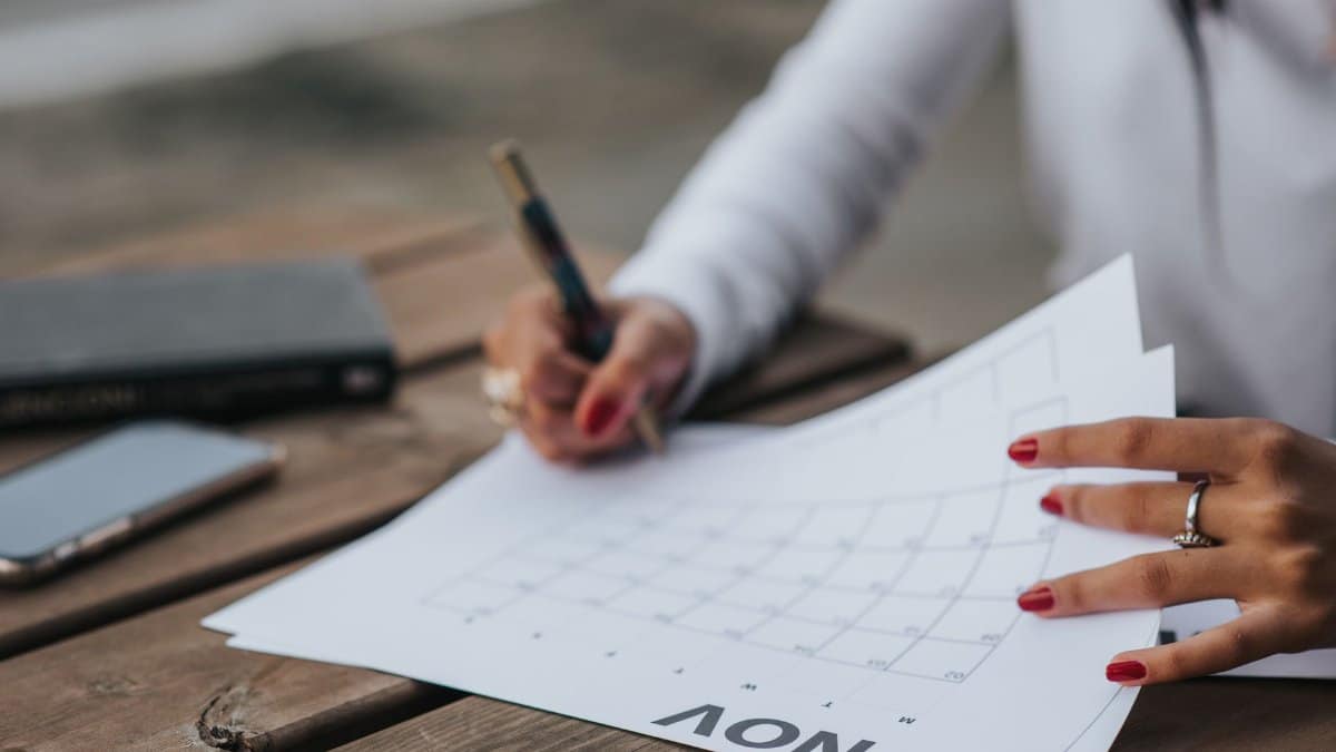 Crop faceless female in white blouse making plans for month while sitting at wooden table in park