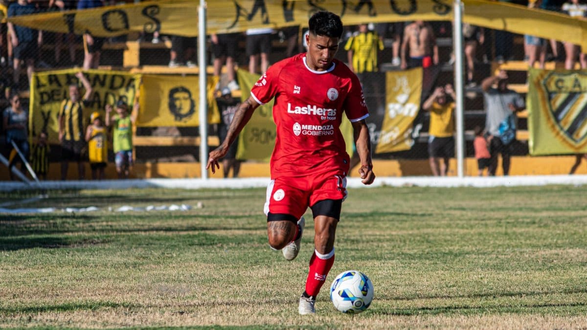A soccer player in red uniform dribbling during a daytime match with spectators.