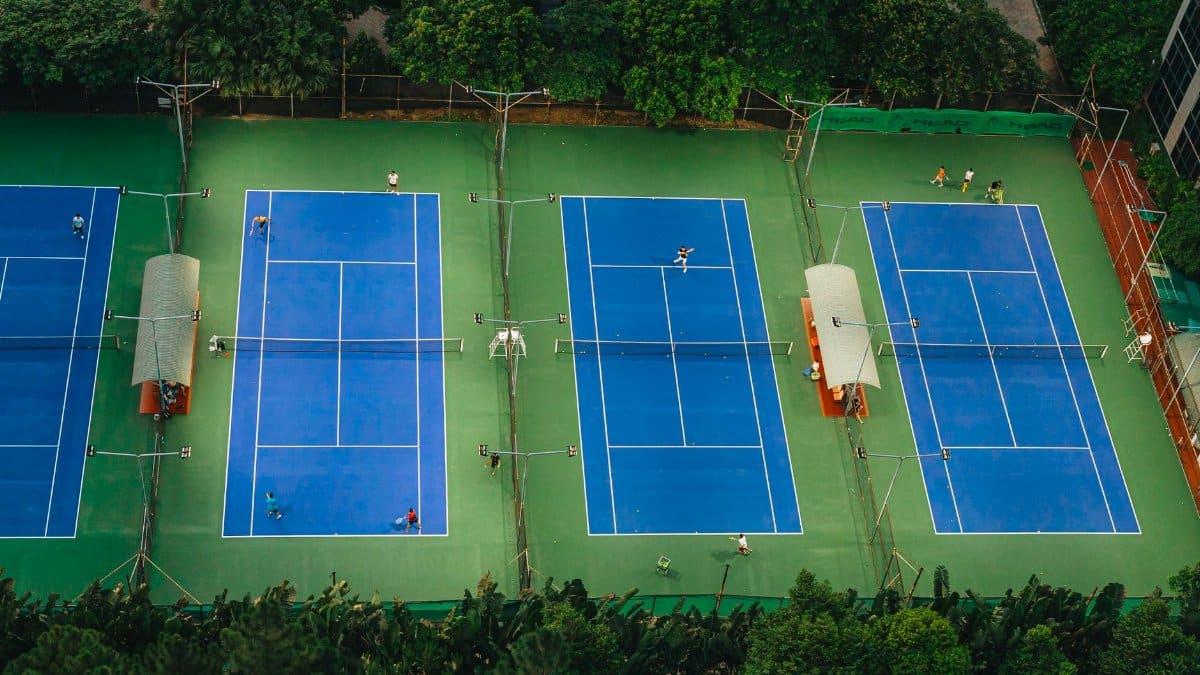 Tennis courts from above showcasing players in action, surrounded by greenery.
