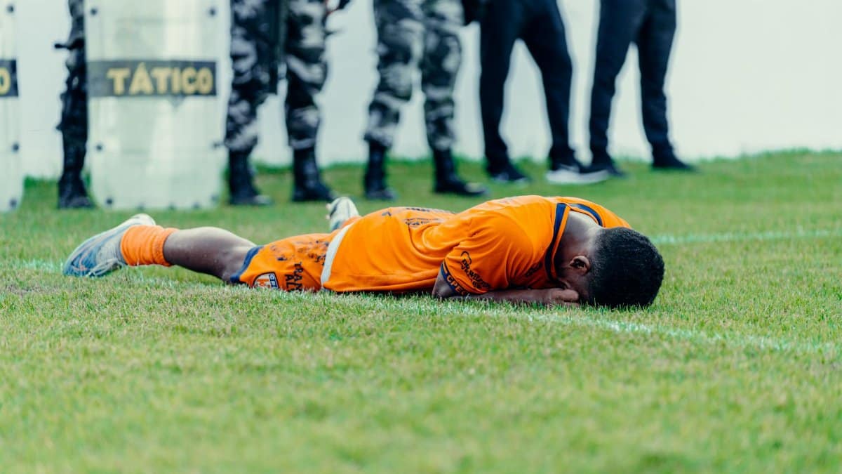Injured football player in orange jersey lying on field with police presence.
