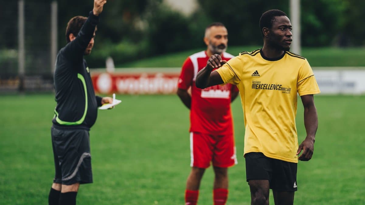Referee issuing a red card to a soccer player in an outdoor match setting.