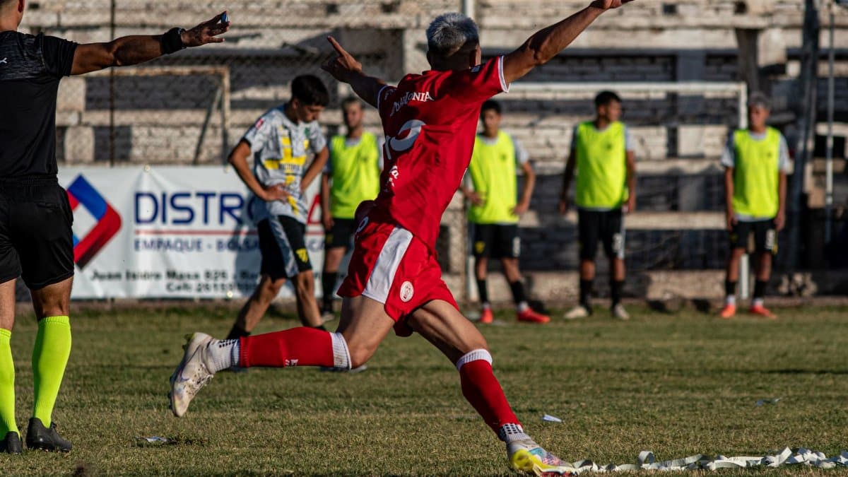 A soccer player in red celebrates a goal with enthusiasm on an outdoor field.