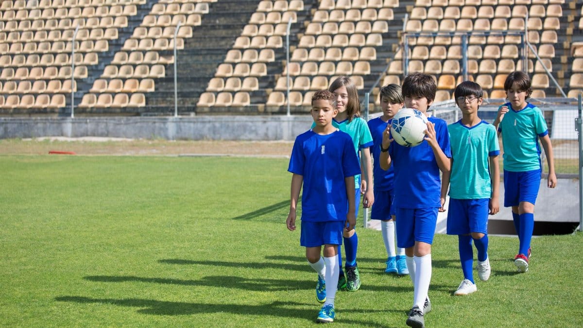 Group of boys in soccer uniforms walking on a grassy field during the day.