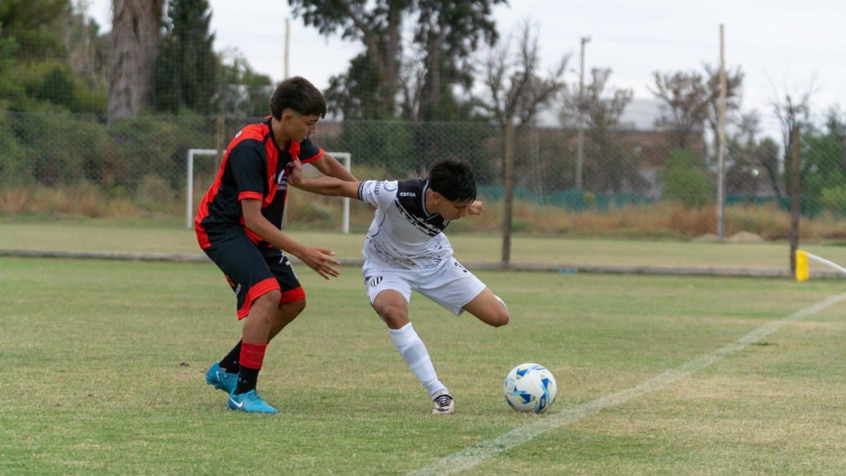 Two teenage soccer players in an intense match on a grassy field.