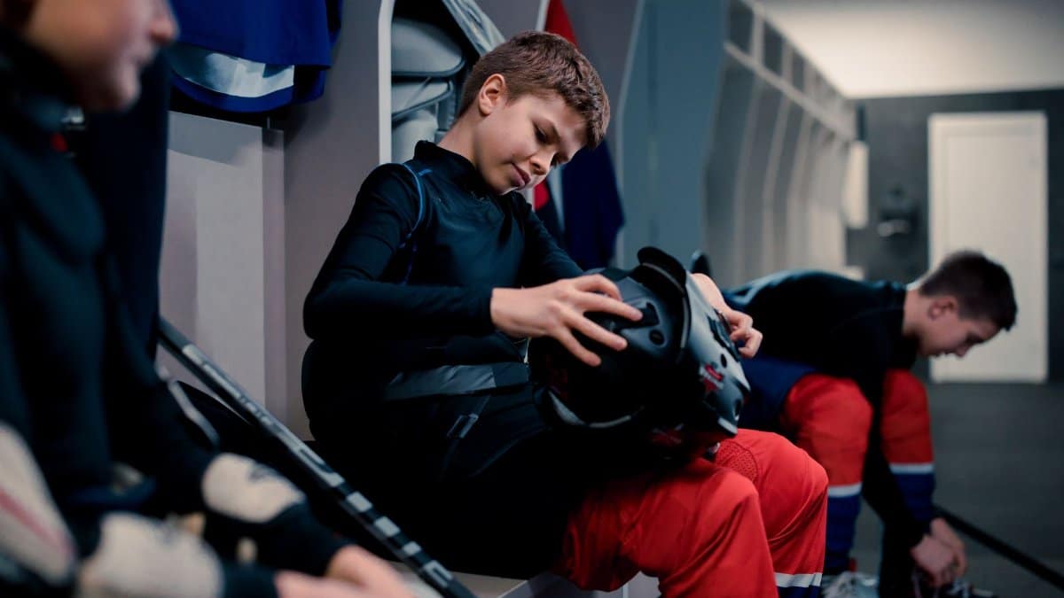 Teen ice hockey players in the locker room, getting ready with safety gear.