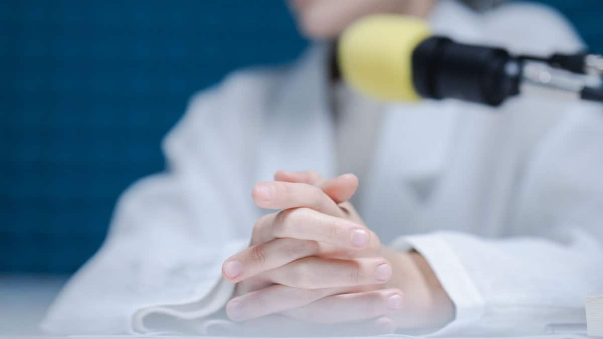 Close-up of hands folded near a microphone in a podcast studio.