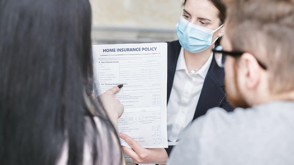 A professional woman explains a home insurance policy to clients during a meeting. Indoors setting.