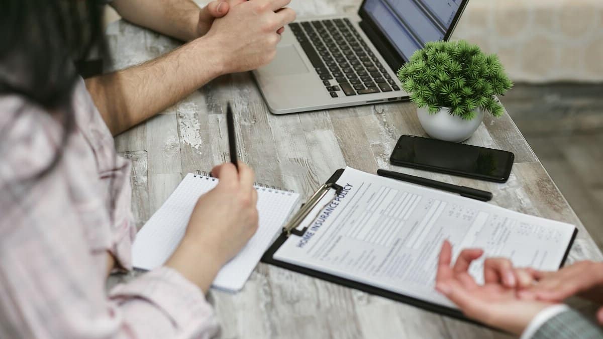 Professionals discussing home insurance policy over laptop and notes in an office setting.