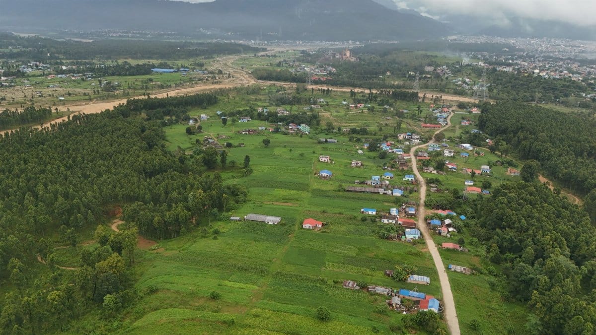 A stunning aerial view showcasing lush green fields and a small village in Nepal, surrounded by trees and hills.