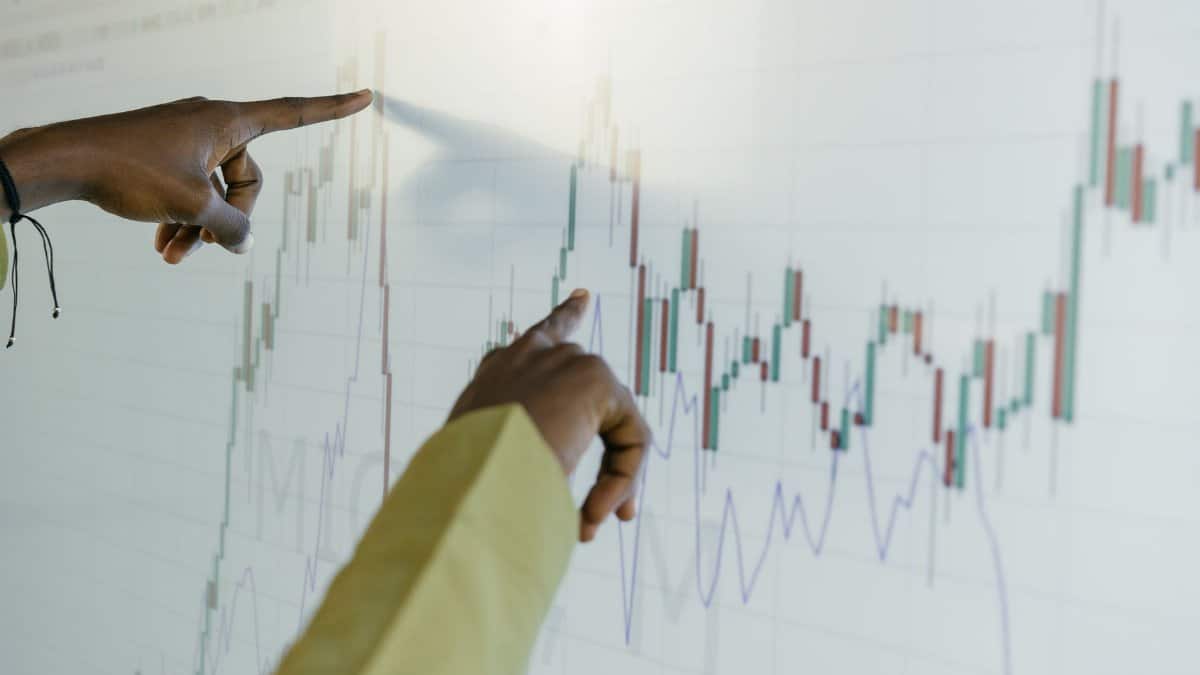 Hands pointing at a financial stock chart on a digital screen, highlighting data analysis and trends.