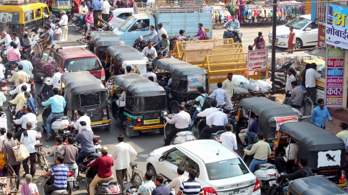 Crowded urban street with cars, bikes, and auto rickshaws in bustling city traffic.