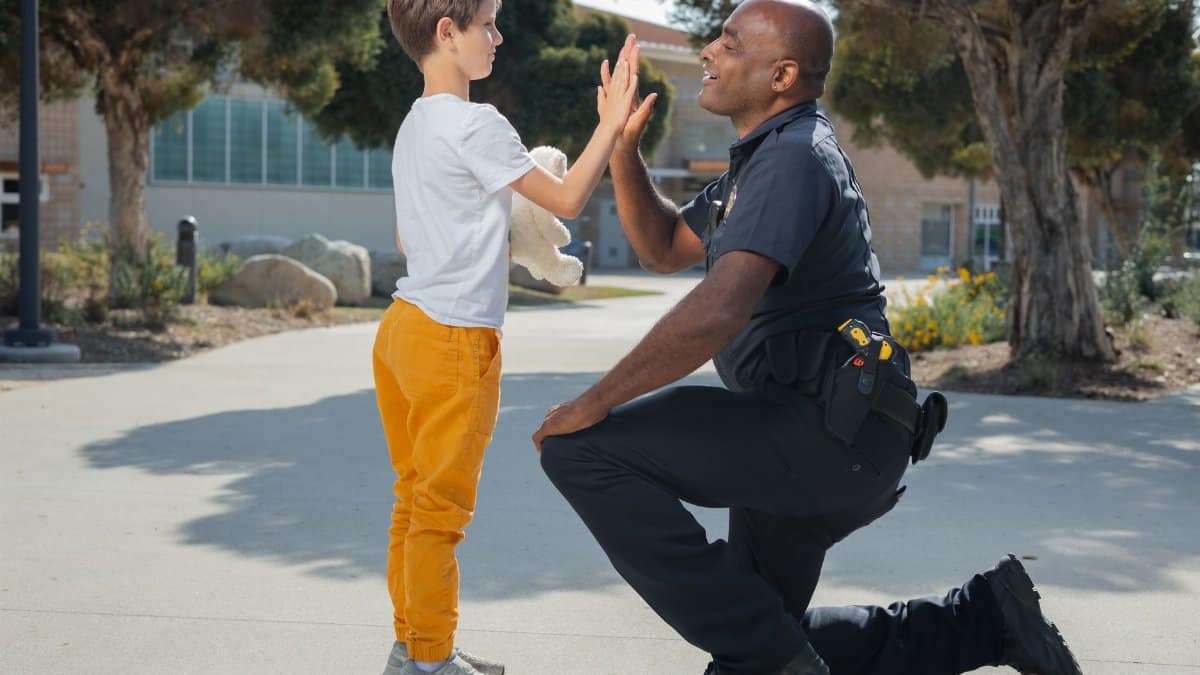 Police officer and young boy high-five outdoors, symbolizing trust and community connection.