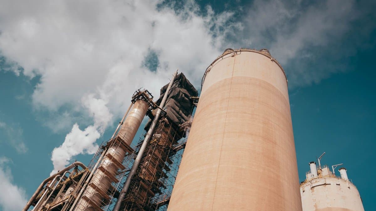Industrial factory towers emit smoke against a vibrant blue sky, highlighting environmental concerns.