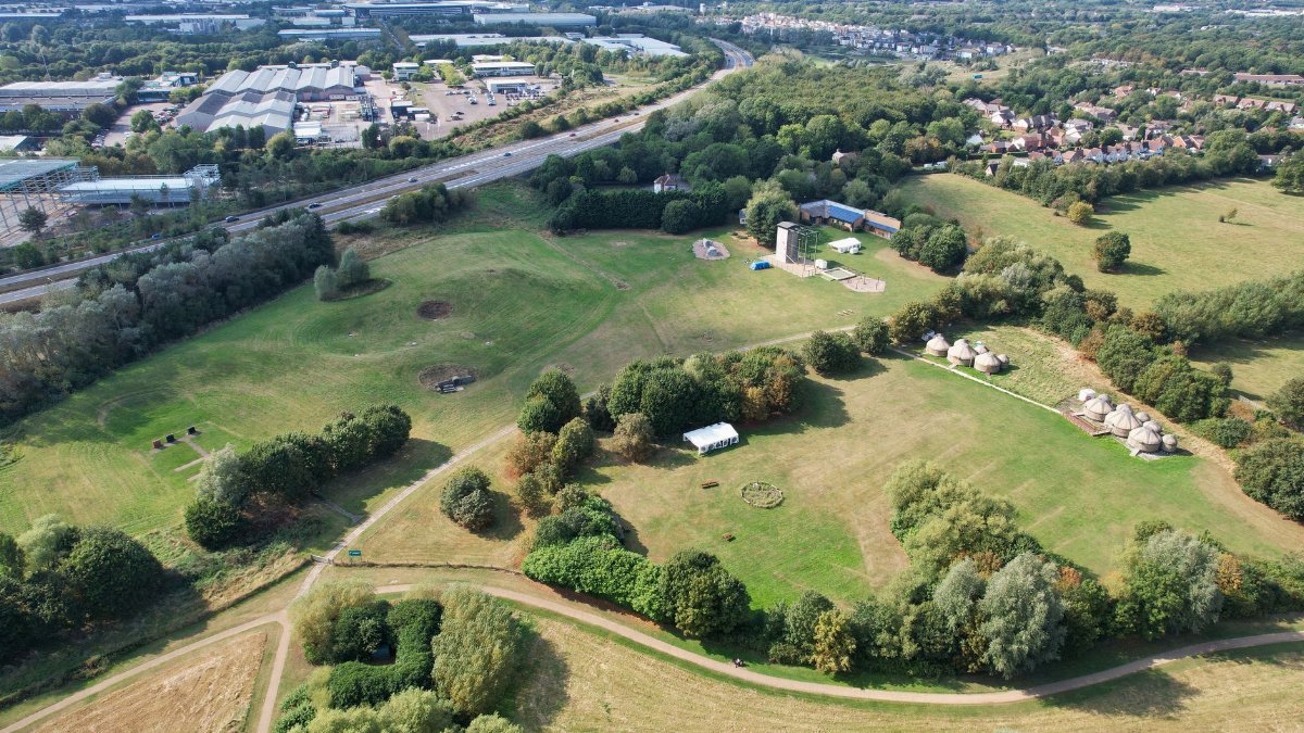 Aerial shot of green countryside landscape in Milton Keynes, England, featuring fields, trees, and rural buildings.