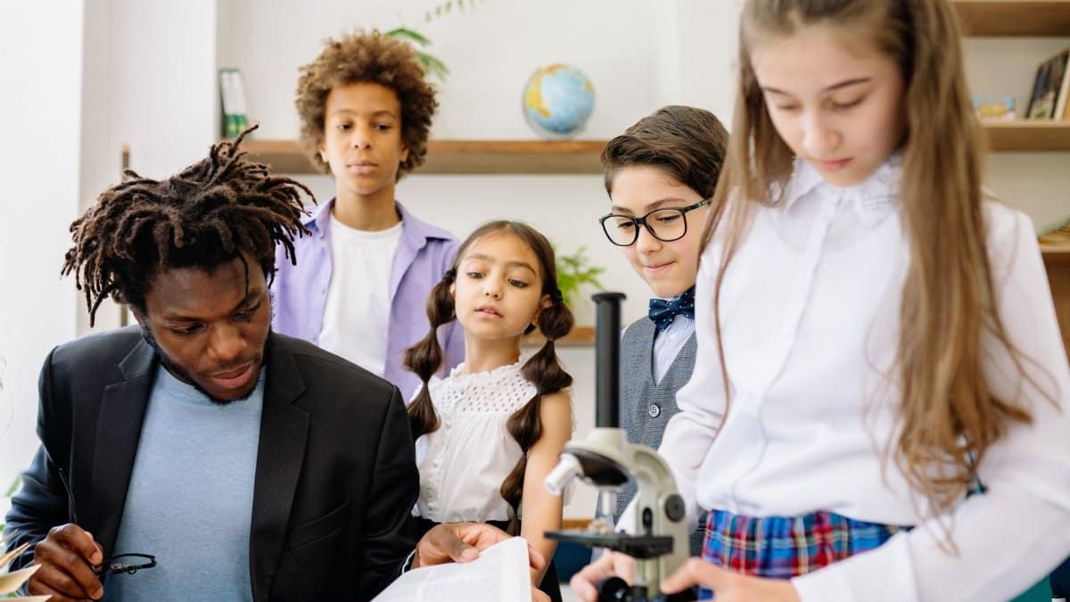A teacher and students in a classroom engaging with a microscope for a science lesson.