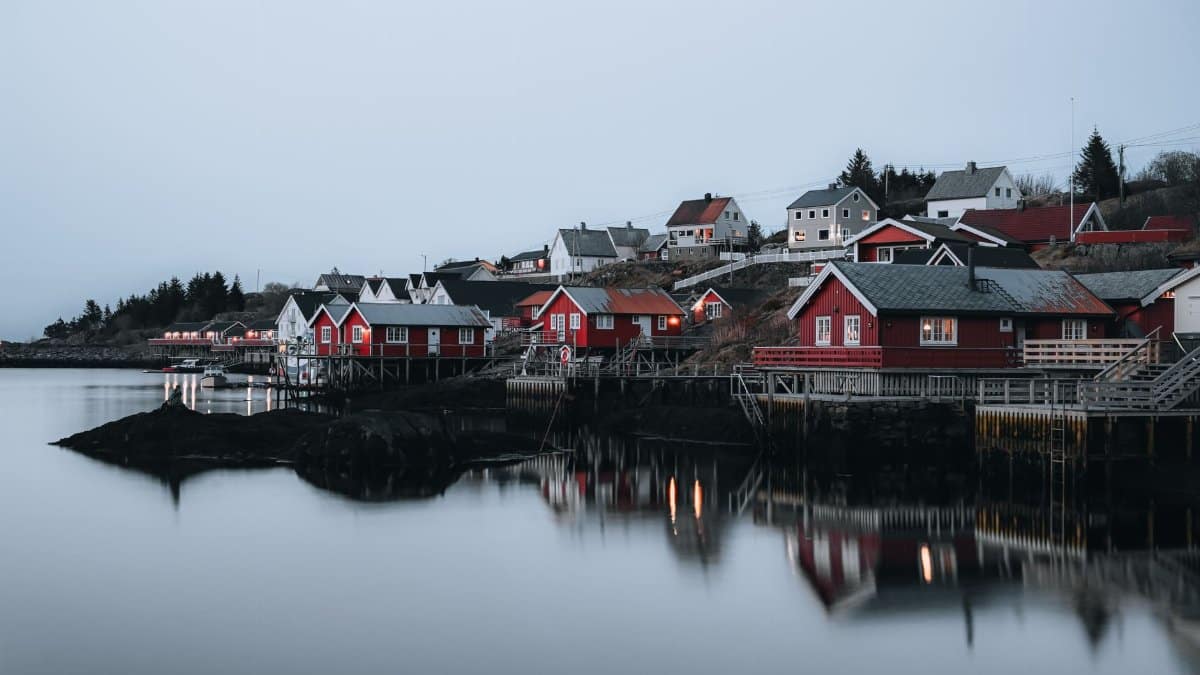 Quaint red wooden houses reflecting in calm water in Nordland, Norway during twilight.