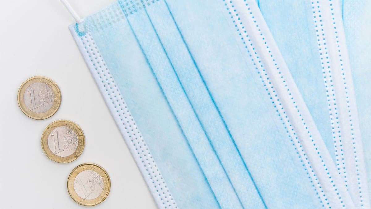 Flatlay of surgical face masks and euro coins, symbolizing pandemic economic challenges.