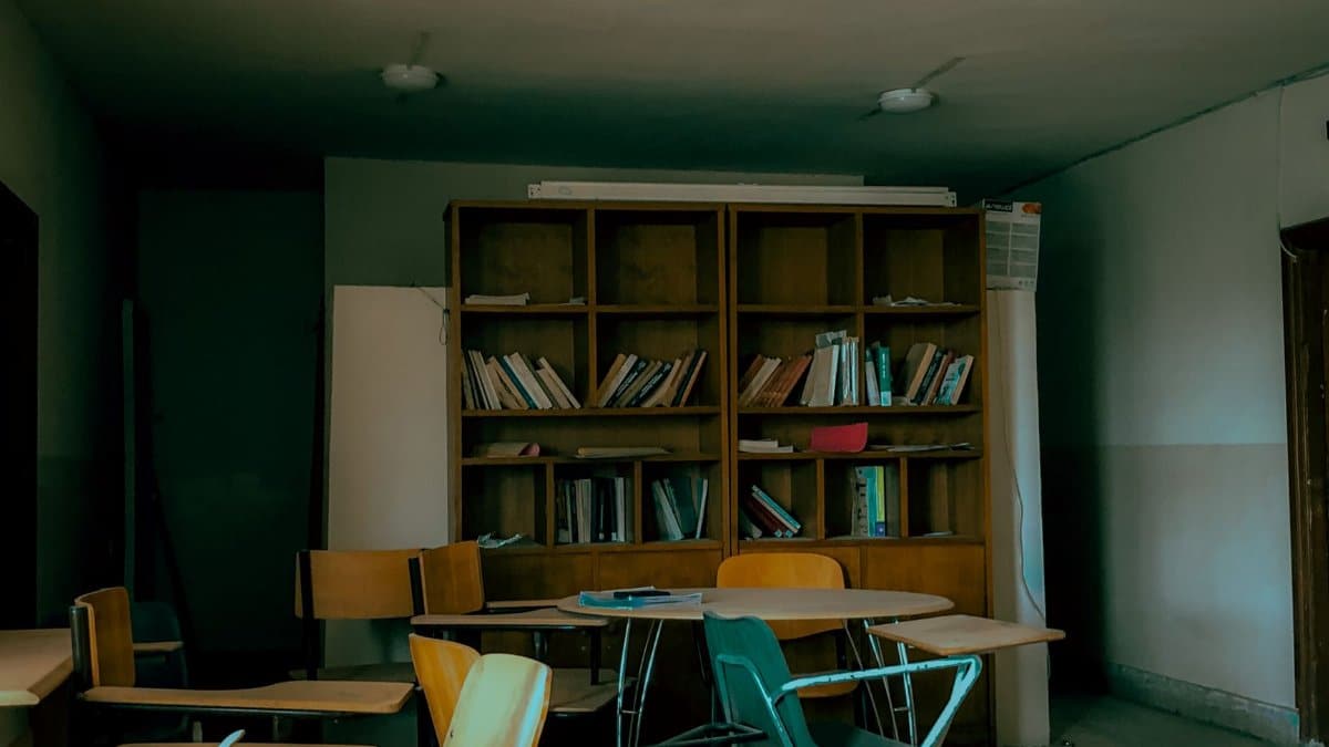 An empty classroom with scattered chairs and a bookshelf full of old books.