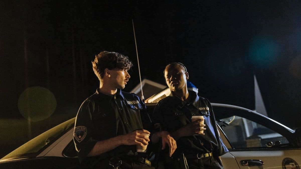 Two police officers in uniform enjoying coffee during a night shift next to their patrol car.