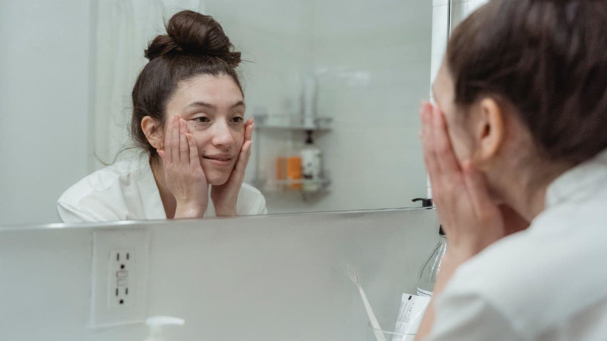Woman applying skincare in front of a mirror, enjoying her morning beauty ritual indoors.