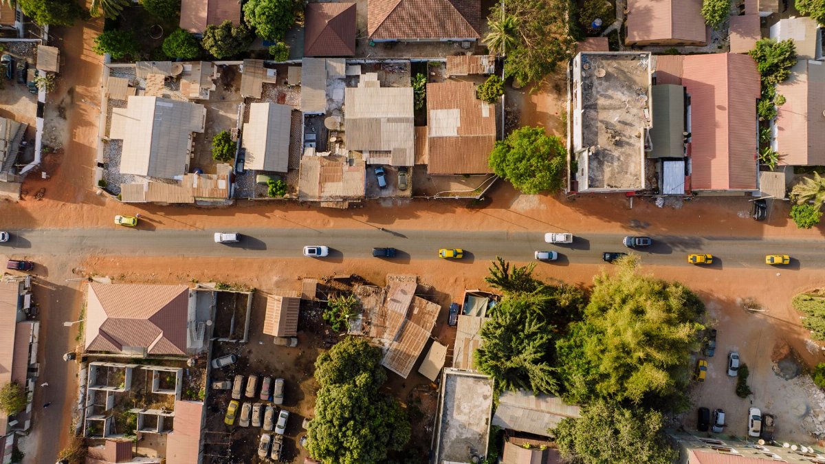 Drone shot of a street with traffic in a village with houses and greenery viewed from above.