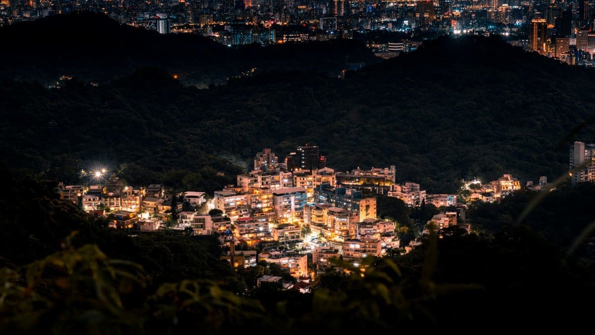 A captivating aerial view of Taipei cityscape and illuminated urban area at night, surrounded by lush hills.