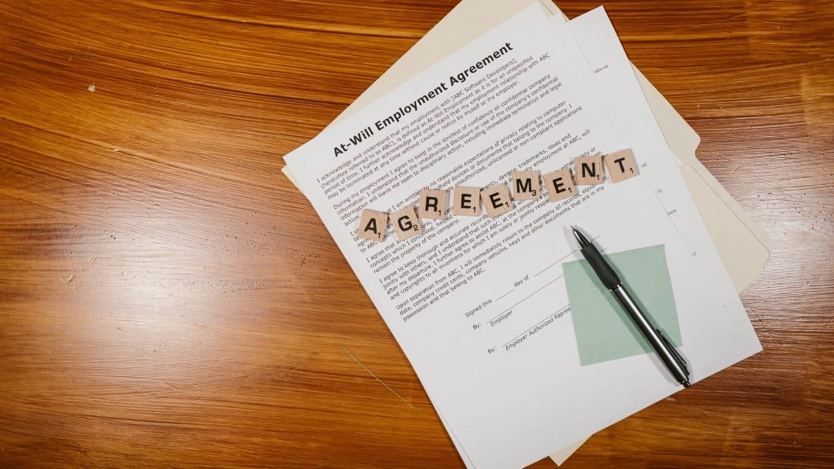 A flat lay of an employment agreement with Scrabble tiles on a wooden table.