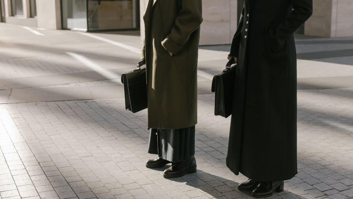 Two business professionals standing outdoors with briefcases, exuding elegance and professionalism.