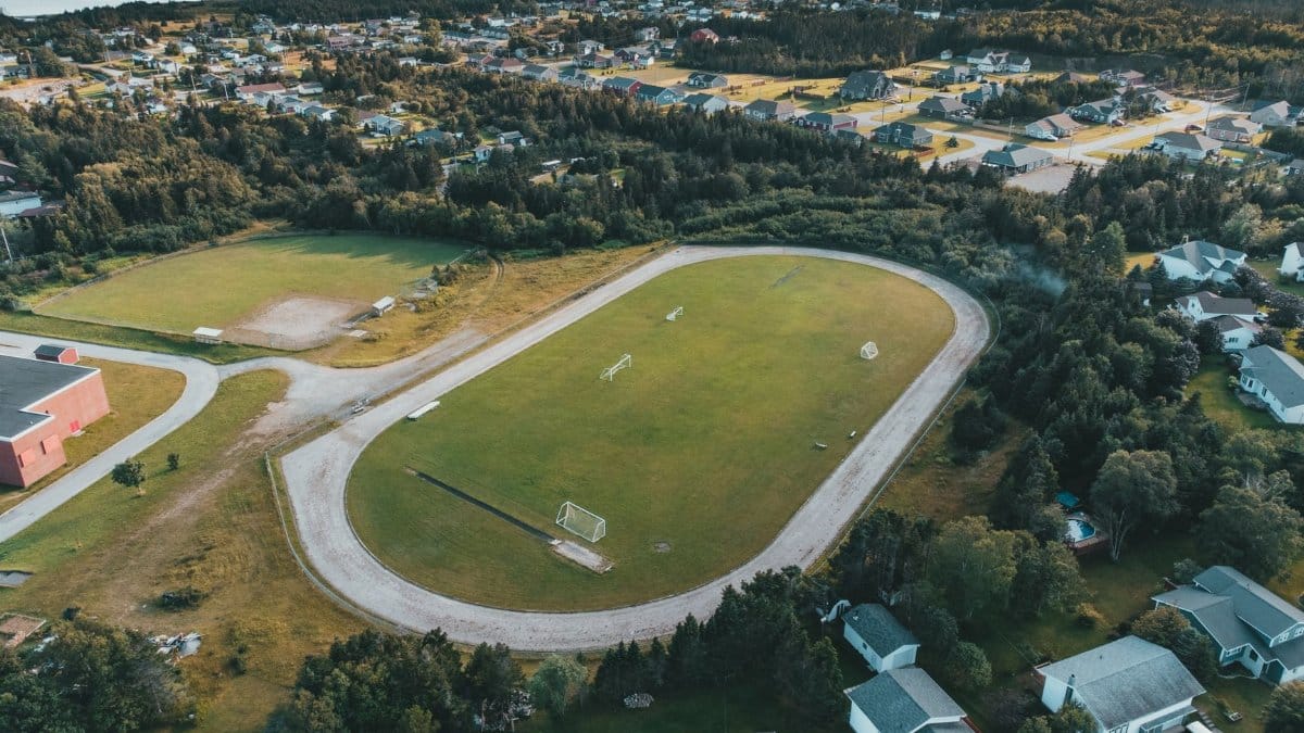 Scenic aerial view of a soccer field surrounded by a suburban neighborhood with lush green trees.