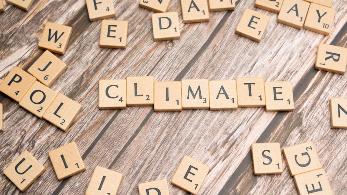 Wooden Scrabble tiles arranged to spell 'CLIMATE' on a wooden surface.