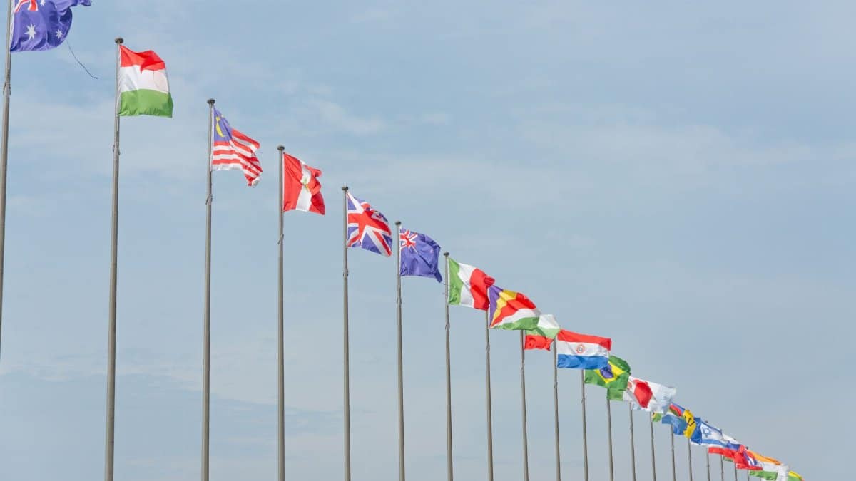 A series of international flags flying in a line against a clear blue sky, symbolizing global unity.