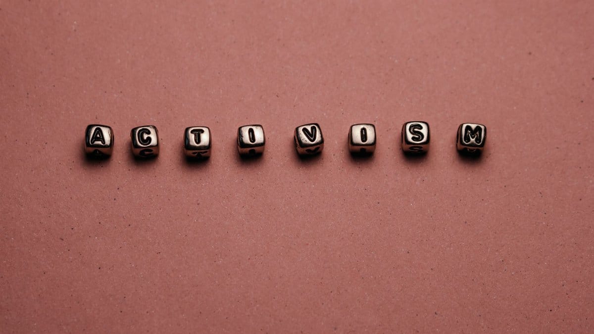 Close-up of metal beads spelling 'Activism' against a pink background, emphasizing activism themes.
