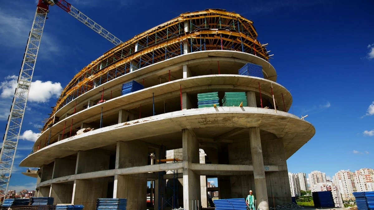 Low angle view of a circular building under construction with a crane, clear blue sky.