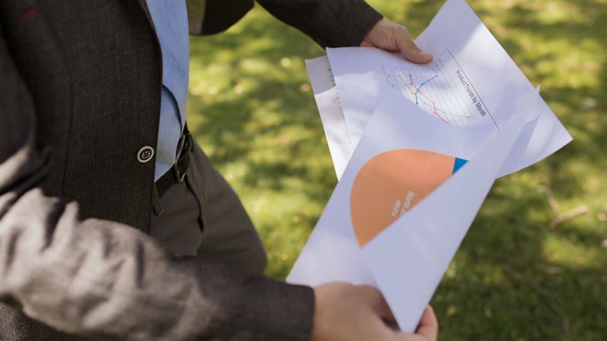 Man in suit holding financial reports in a sunny park.