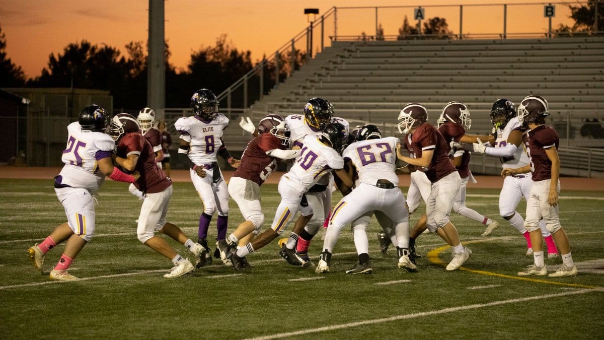 Exciting high school football game with players in action on a field at sunset.