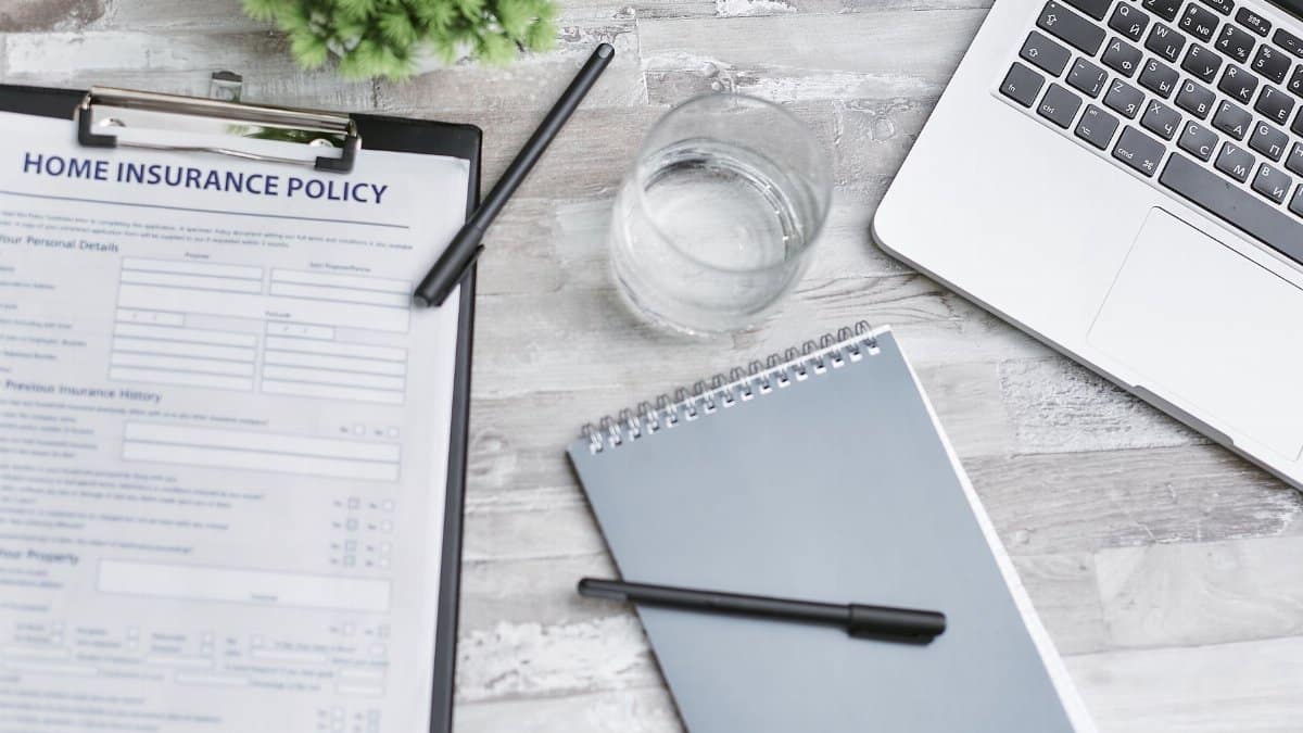 Flat lay of a workspace with a home insurance policy, laptop, and notebook on a desk.