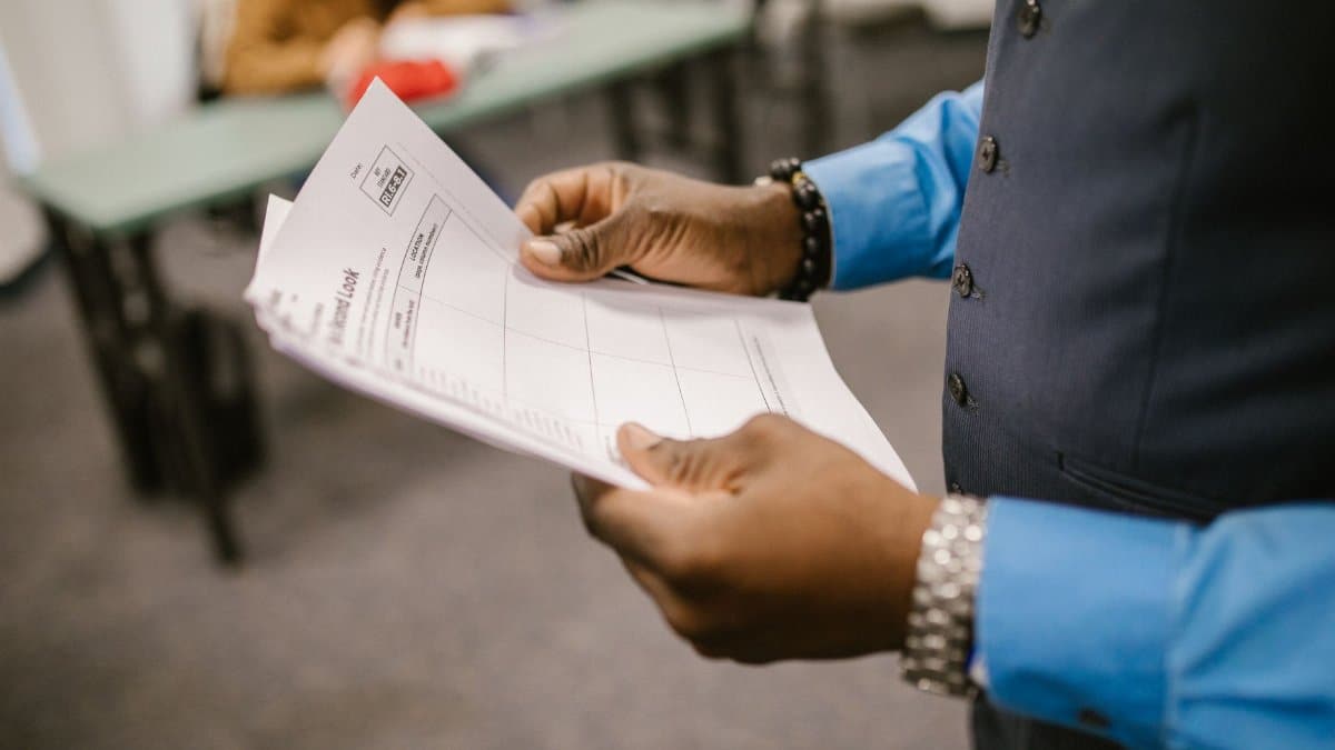 An instructor examining test papers in a classroom setting, focusing on education and evaluation.