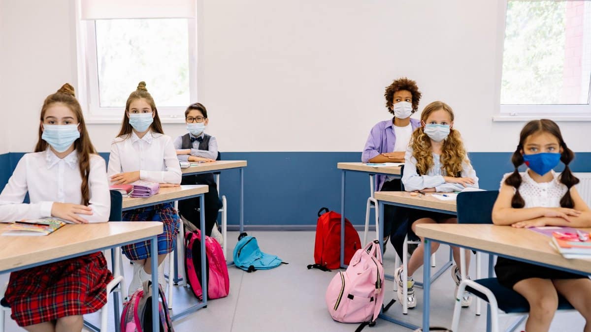 Students in masks seated at desks in a classroom, maintaining safety measures.