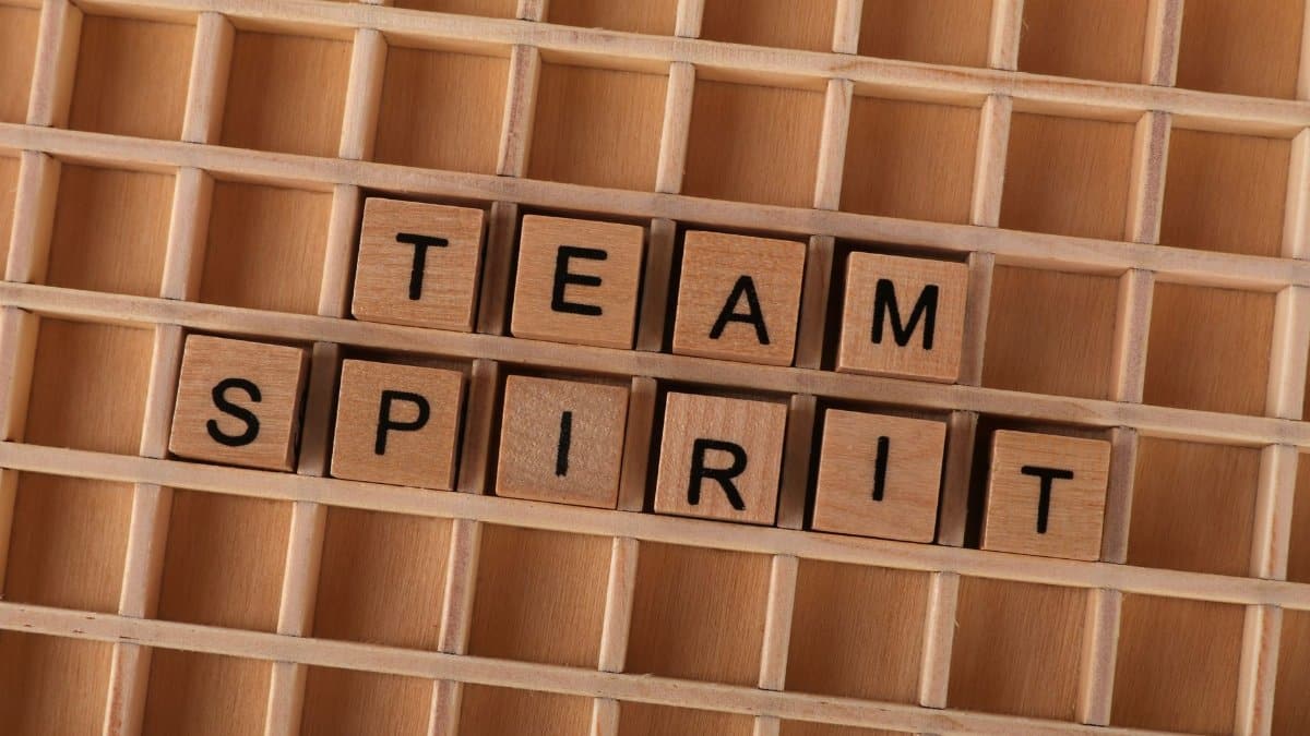 Wooden Scrabble tiles arranged to spell 'Team Spirit' on a wooden grid.