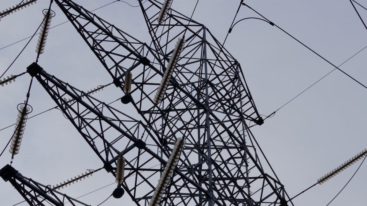 Low angle shot of a metal power transmission tower with cables against a clear sky.
