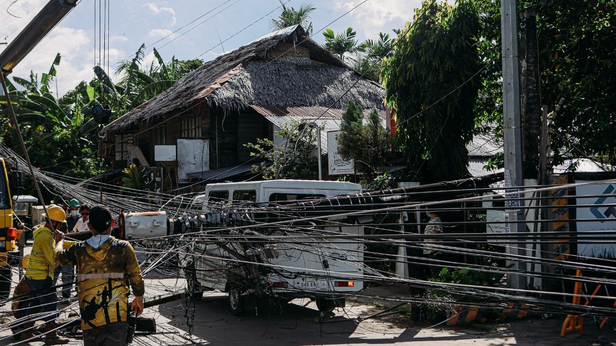 Workers fix tangled power lines after an accident involving a vehicle in a tropical location.